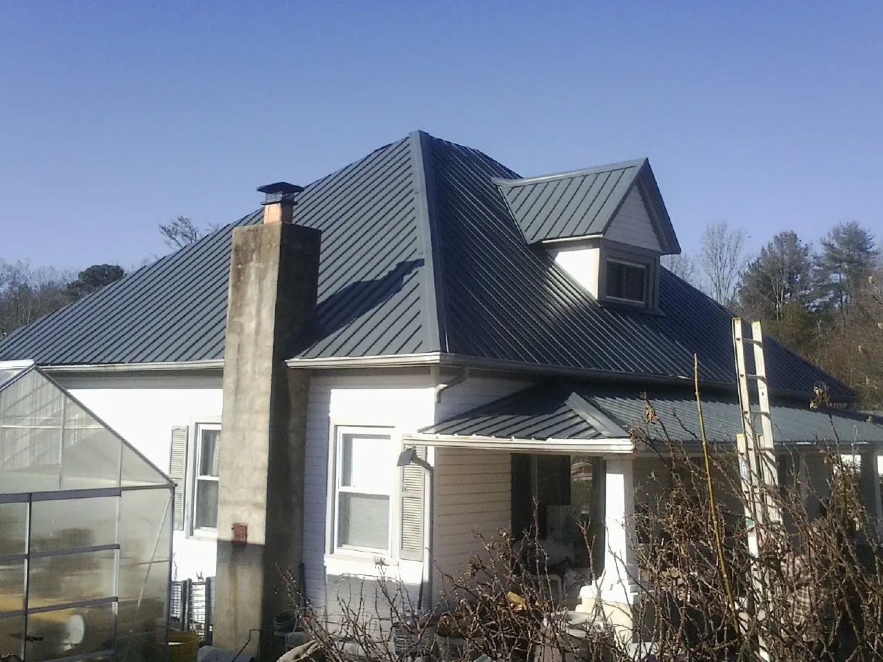 Dark blue standing seam metal roof on a white farmhouse with dormer — Slate & Tile Roof Repair by Roofing Brothers in Port Huron