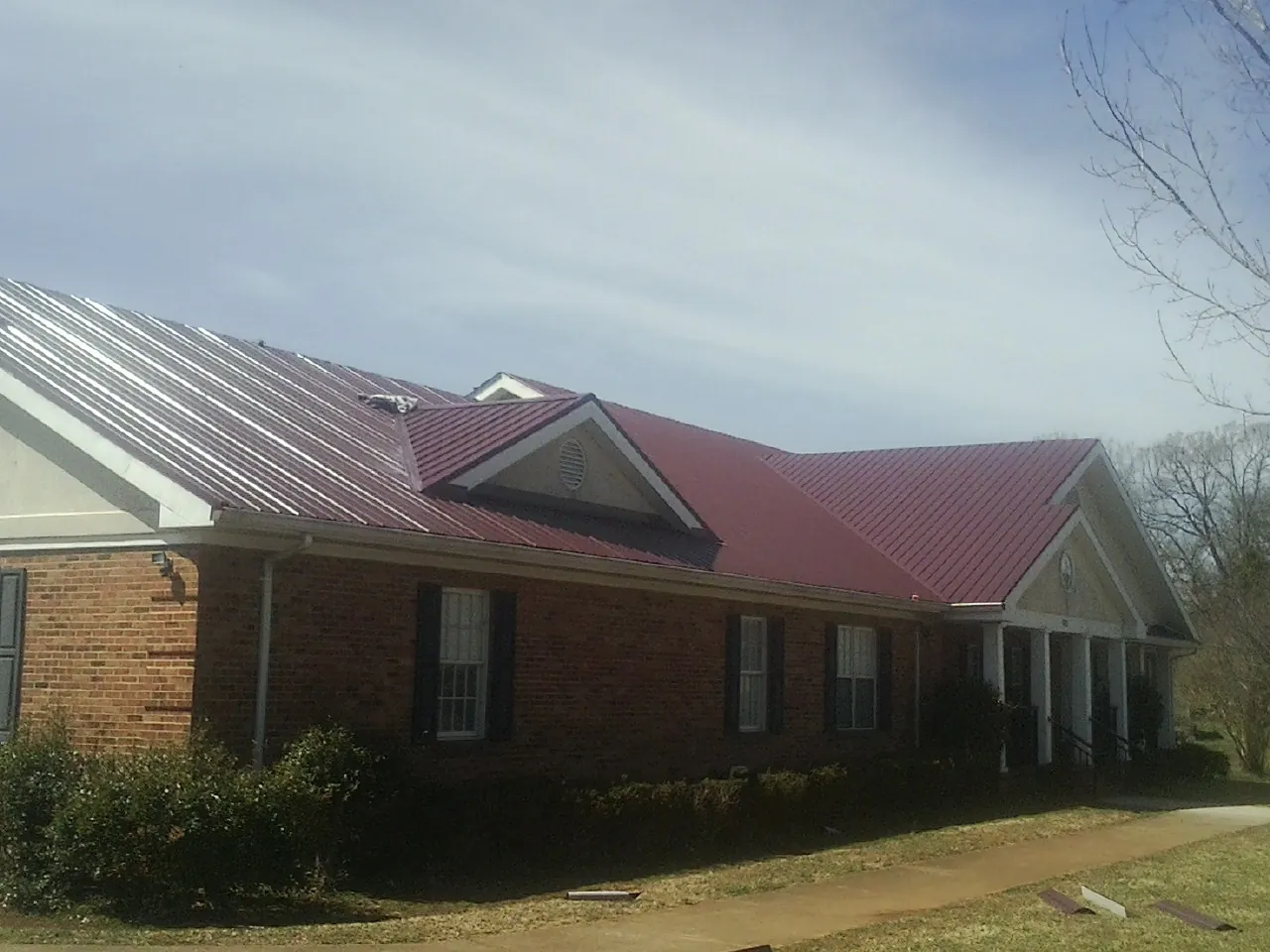 Red metal roof with gabled entries on a long brick building, from a Hail Damage Roof Repair job in Port Huron