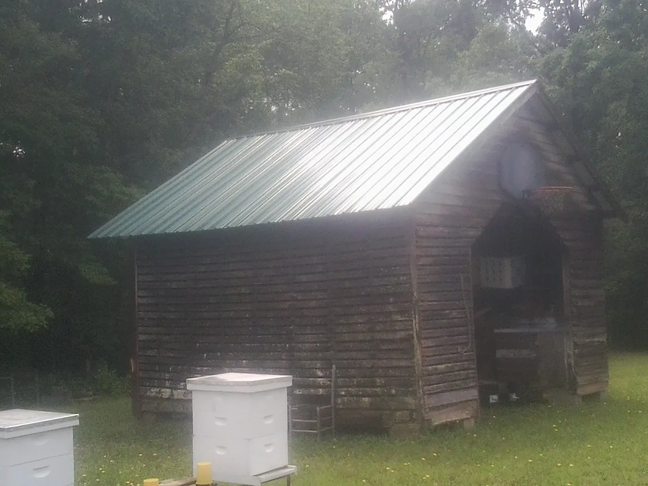 Green metal roof on a weathered barn beside stacked beehives in Port Huron