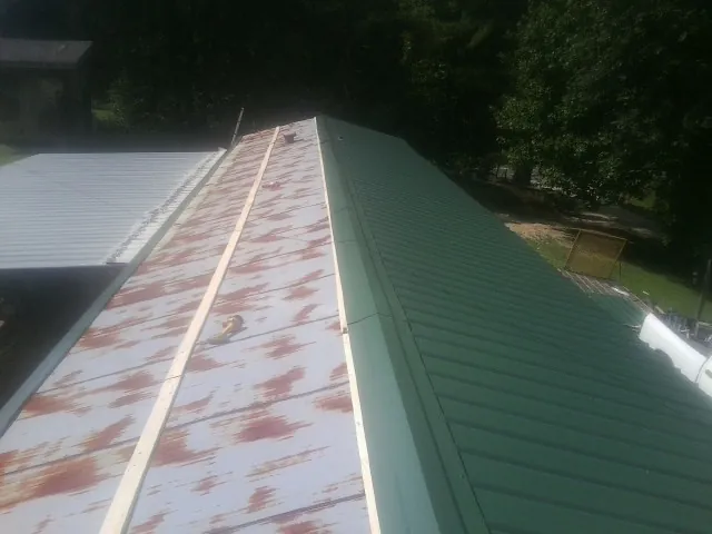 Old rusted panels beside newly installed green metal roofing — Wind Damage Roof Repair by Roofing Brothers in Port Huron