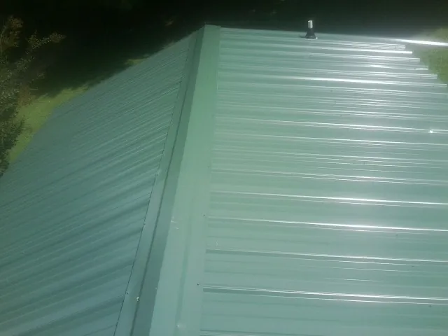 New green metal panels meeting at the ridge of a roof — Flat Roof Repair work by our crew in Port Huron