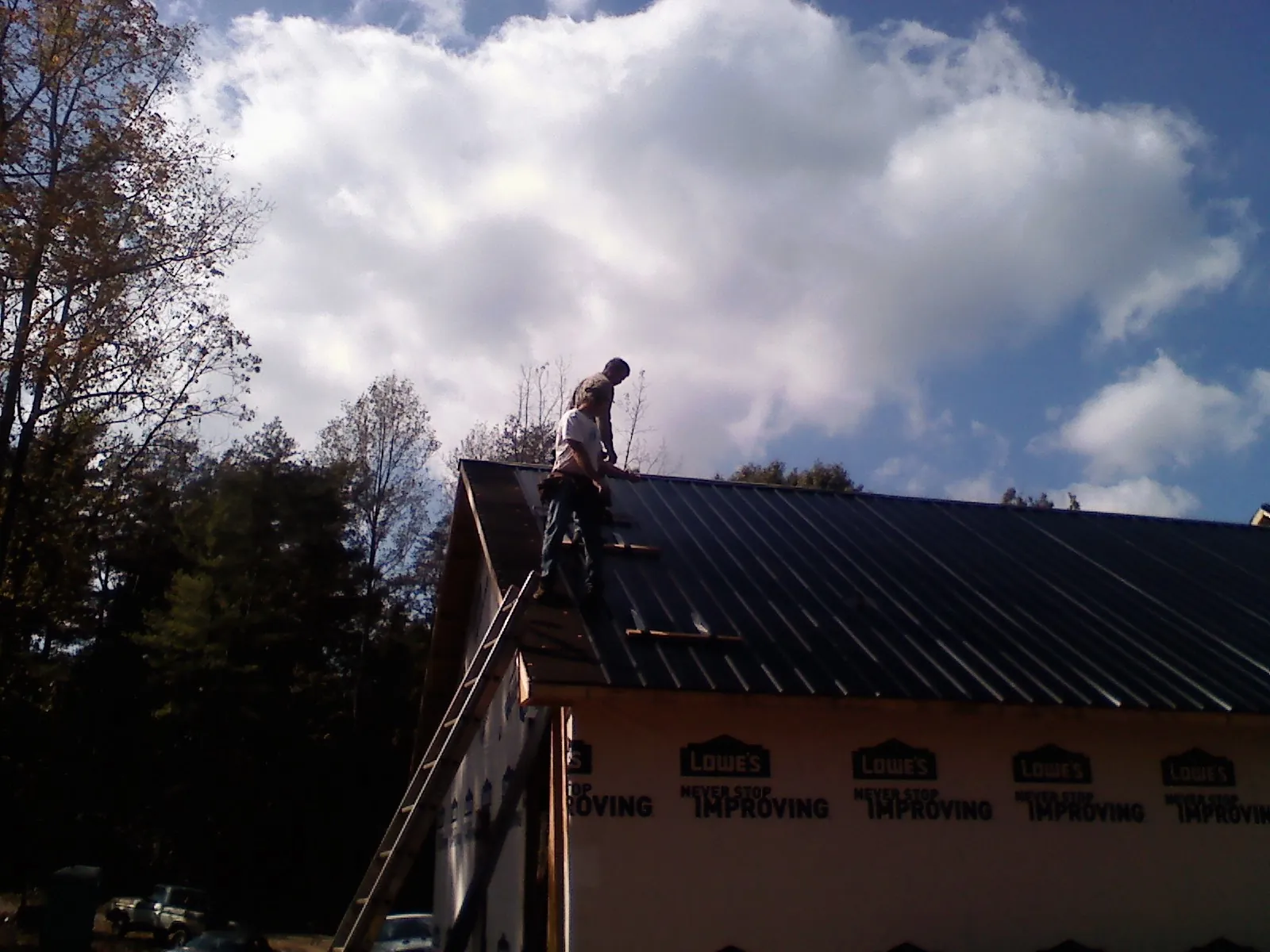 Roofer fastening dark metal panels high against a cloudy sky, from a Roof Inspection job in Port Huron
