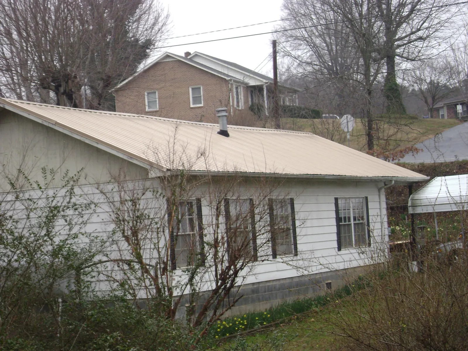 Tan metal roof on a white sided house set into a hillside — Commercial Roofing by Roofing Brothers in Port Huron